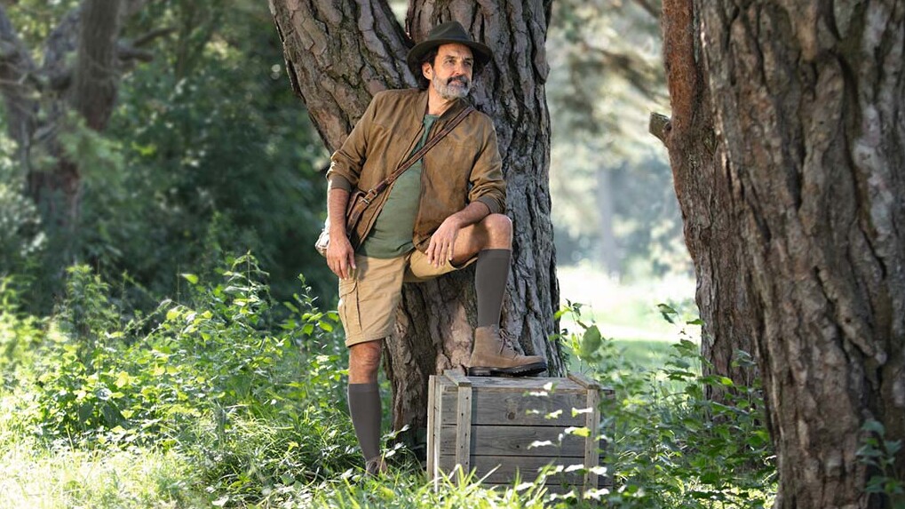 Ein Mann mit Entdecker-Outfit steht in der Natur und schaut in die Ferne. Er trägt kniehohe Kompressionsstrümpfe. Ein Mann mit Entdecker-Outfit steht in der Natur und schaut in die Ferne. Er trägt kniehohe Kompressionsstrümpfe.