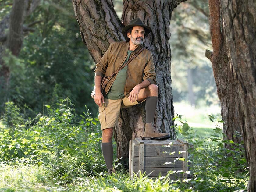 Ein Mann mit Entdecker-Outfit steht in der Natur und schaut in die Ferne. Er trägt kniehohe Kompressionsstrümpfe. Ein Mann mit Entdecker-Outfit steht in der Natur und schaut in die Ferne. Er trägt kniehohe Kompressionsstrümpfe.