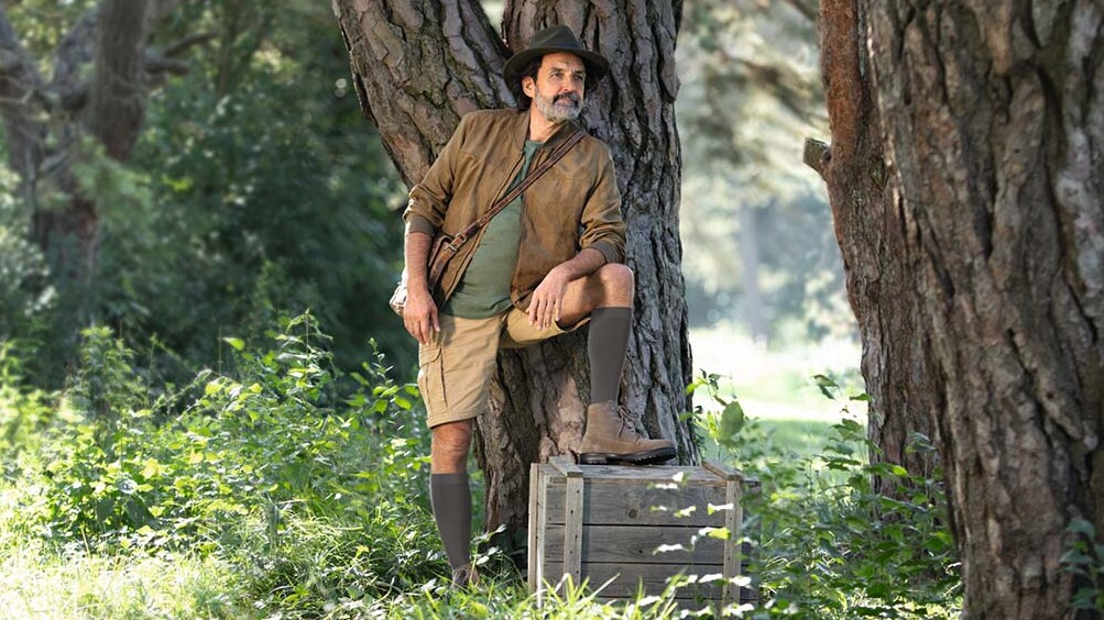Ein Mann mit Entdecker-Outfit steht in der Natur und schaut in die Ferne. Er trägt kniehohe Kompressionsstrümpfe. Ein Mann mit Entdecker-Outfit steht in der Natur und schaut in die Ferne. Er trägt kniehohe Kompressionsstrümpfe.