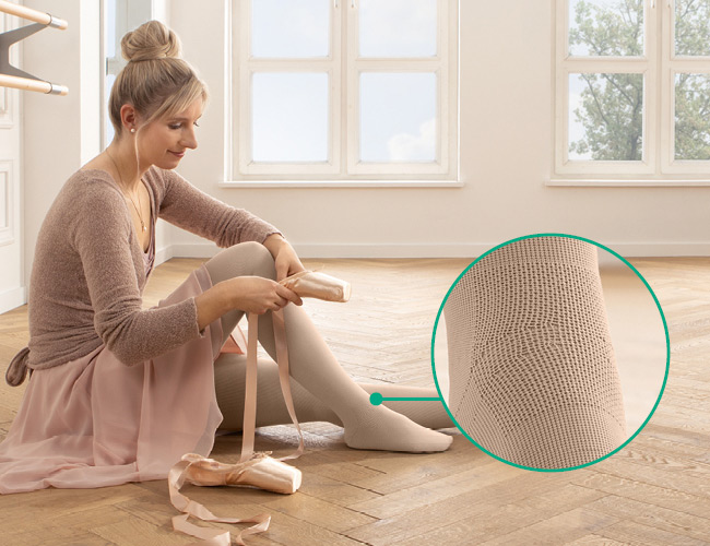 zone fonctionnelle Cou-de-pied Femme en tenue de danseuse avec Juzo Expert et zone fonctionnelle Cou-de-pied assise par terre, en train d'enfiler ses pointes