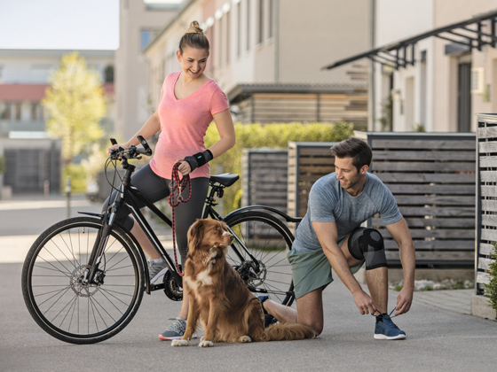 Arthrose Eine Frau und ein Mann führen einen Hund Gassi mit einem Fahrrad
