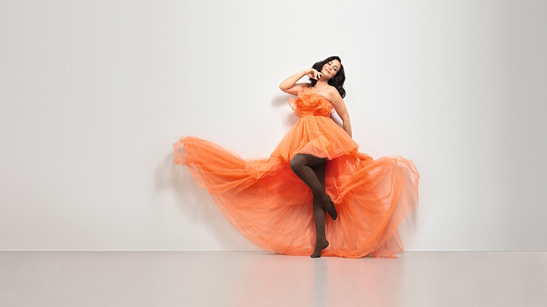 A woman in an orange dress. She is wearing Juzo Inspiration brown tights. A woman in an orange dress. She is wearing Juzo Inspiration brown tights.