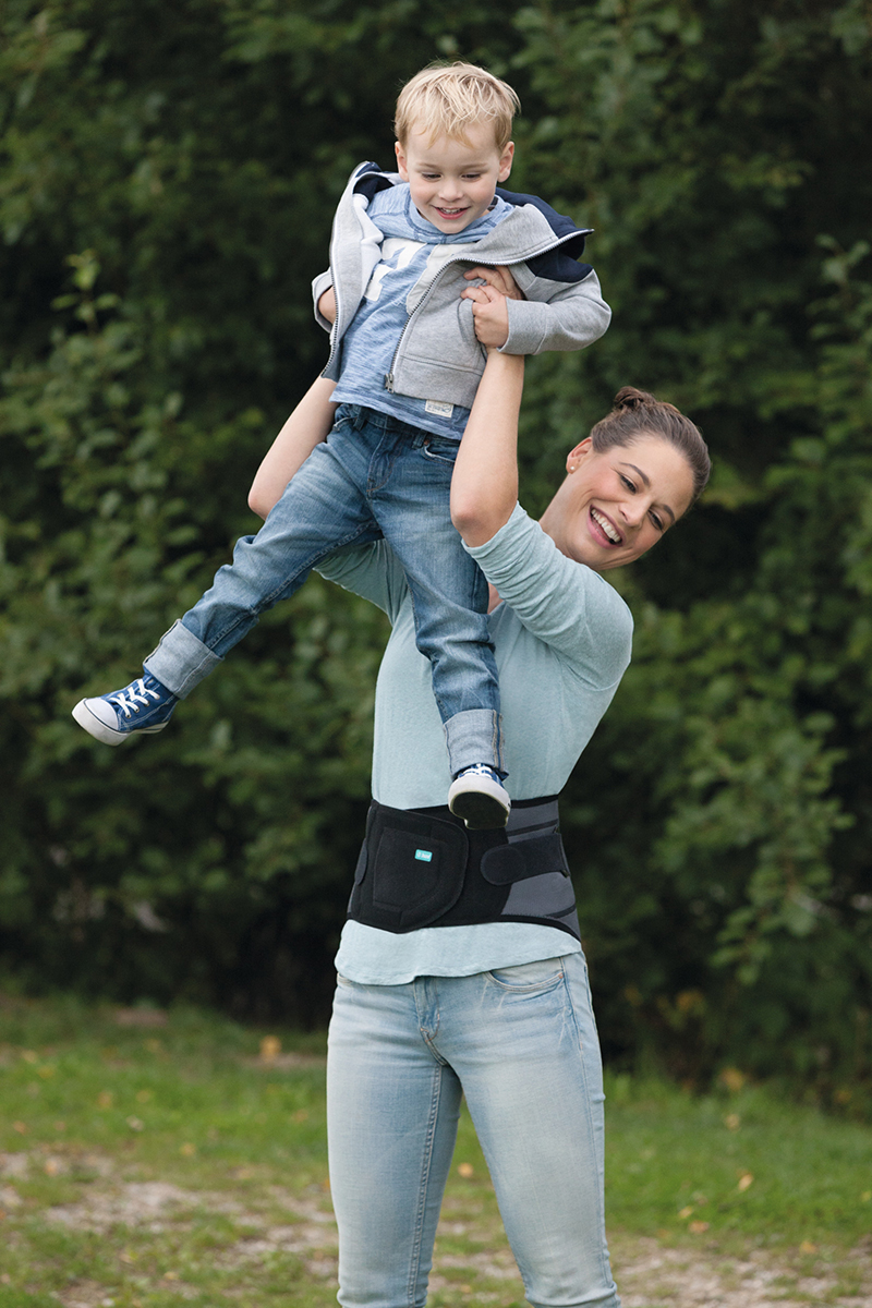 A woman is playing with her son. She is wearing a Juzo back brace.