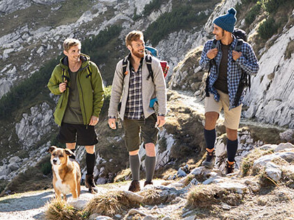 Juzo Adventure Three men with a dog in the mountains. The men are wearing compression stockings on their lower legs.