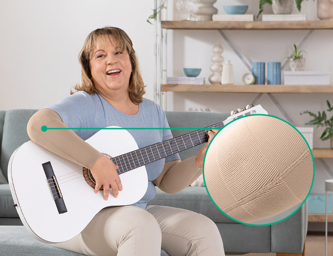 zone fonctionnelle Coude Femme avec Juzo Expert et zone fonctionnelle Coude assise sur un canapé, en train de jouer de la guitare