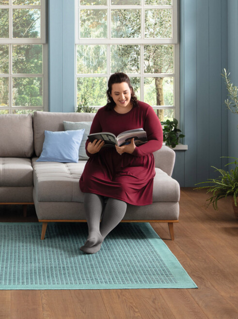 Lifestyle Image Juzo Sensation Fit Woman sitting on her couch, smiling and reading a magazine