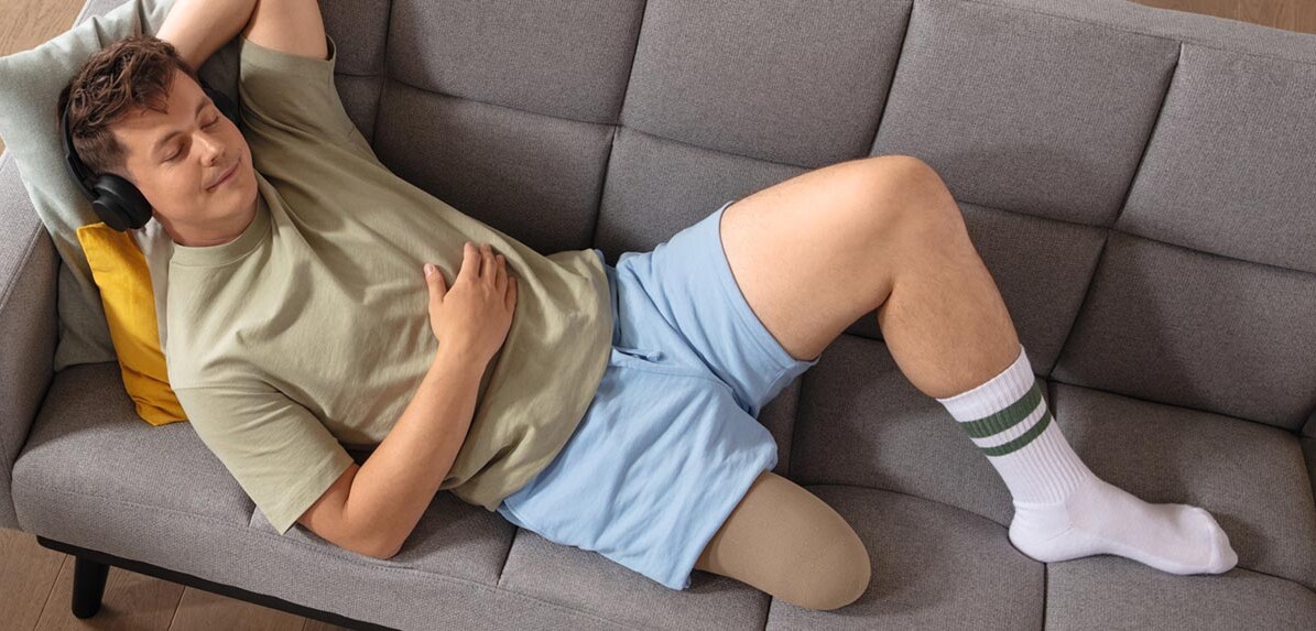 Ung mand bærer den patenterede Juzo Classic Seamless stumpstrømpe, mens han ligger på sofaen uden protese