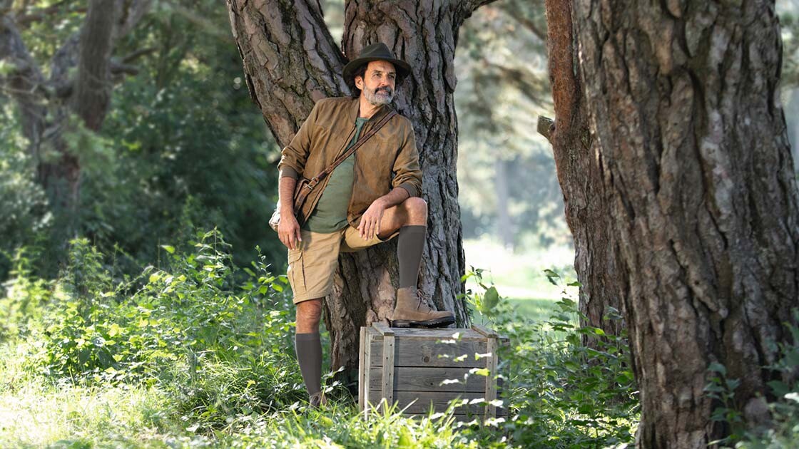 Ein Mann mit Entdecker-Outfit steht in der Natur und schaut in die Ferne. Er trägt kniehohe Kompressionsstrümpfe. Ein Mann mit Entdecker-Outfit steht in der Natur und schaut in die Ferne. Er trägt kniehohe Kompressionsstrümpfe.