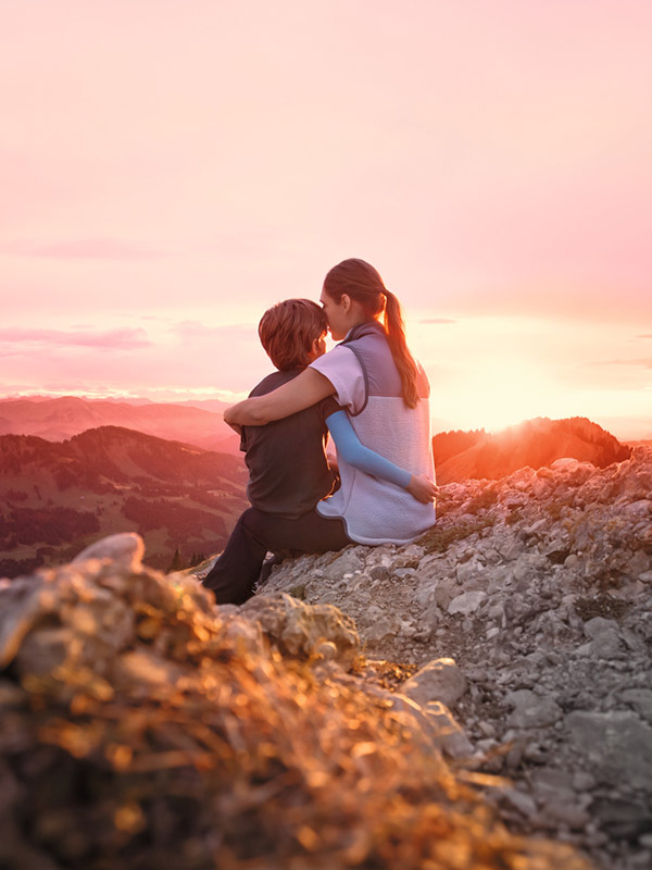 A mother is sitting on a mountain peak with her child. The child is wearing a compression sleeve.