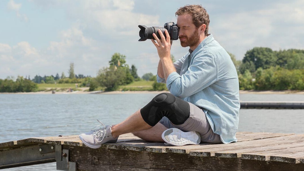 Een fotograaf zit op een steiger. Hij draagt een Juzo-kniebandage Een fotograaf zit op een steiger. Hij draagt een Juzo-kniebandage