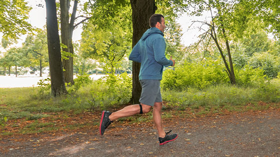 Mann joggt durch Wald und trägt ein Patellasehnenband Mann joggt durch Wald und trägt ein Patellasehnenband