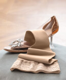 3. Lifestyle image Juzo Soft Juzo Soft Sesame lying on a cushion next to a Cinderella shoe